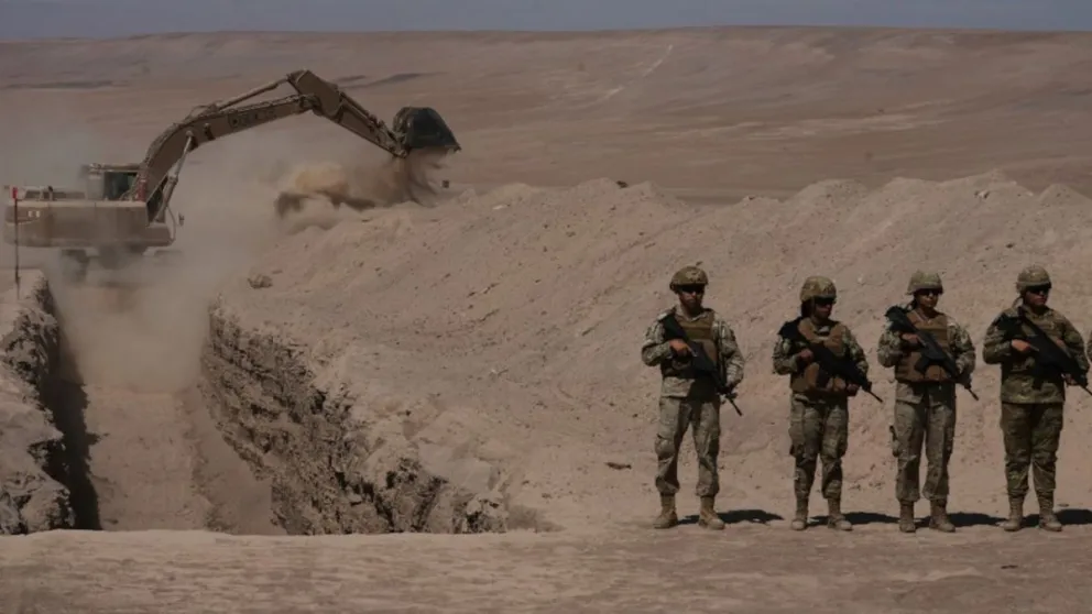 Un grupo de soldados monta guardia junto a una excavadora que cava una zanja para frenar la migración irregular.